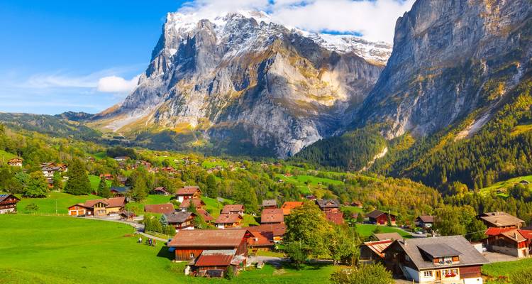 Village pittoresque suisse de chalets en bois niché au pied de falaises calcaires imposantes et de pics enneigés.