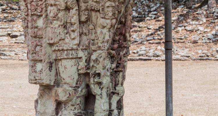 Stèle Maya usée par le temps, sculptée de figures complexes, se dressant sur une place aride