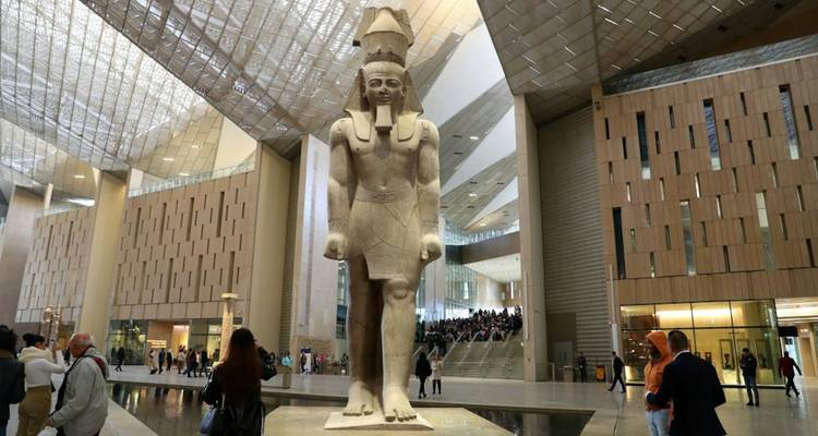 Une statue antique colossale d'un pharaon domine l'atrium spacieux d'un musée moderne bondé de visiteurs.