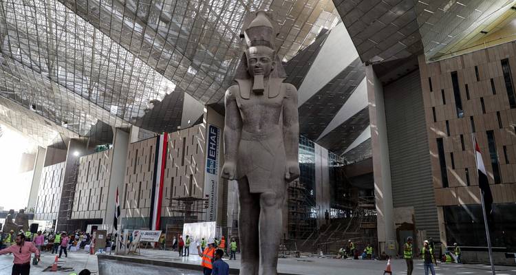 Massive statue pharaonique à l'intérieur d'un chantier de construction à toit de verre d'un musée moderne avec des ouvriers et des échafaudages.