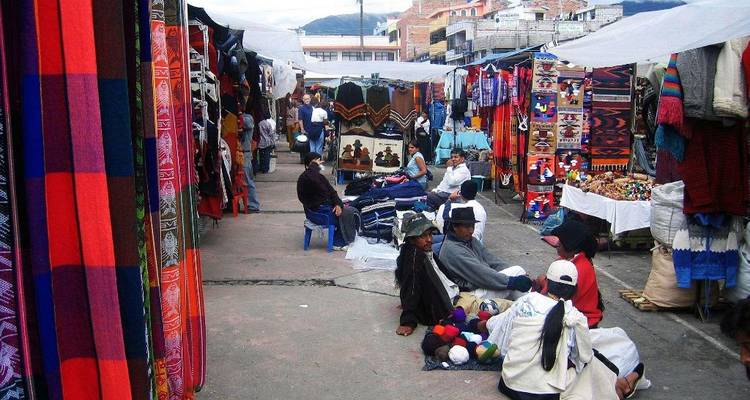 Marché animé d'Otavalo avec des textiles colorés et des clients dans les allées étroites.