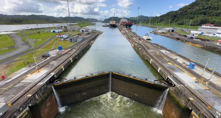 Vista aérea de las compuertas de escluses abriéndose en el Canal de Panamá con barcos esperando y exuberantes colinas al fondo.
