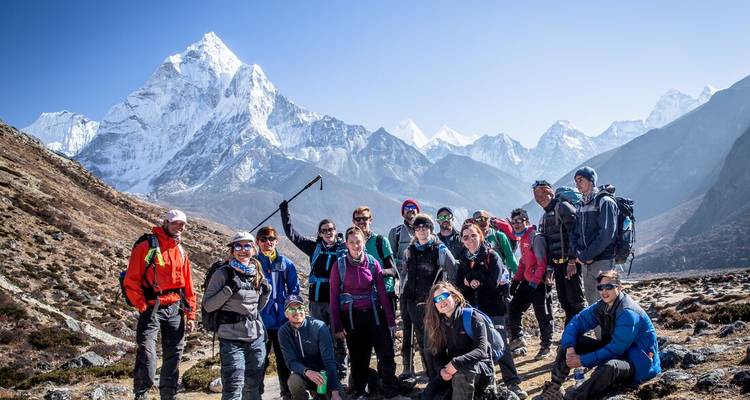 Un gran grupo de trekking posa con bastones de trekking frente a un panorama de picos del Himalaya.