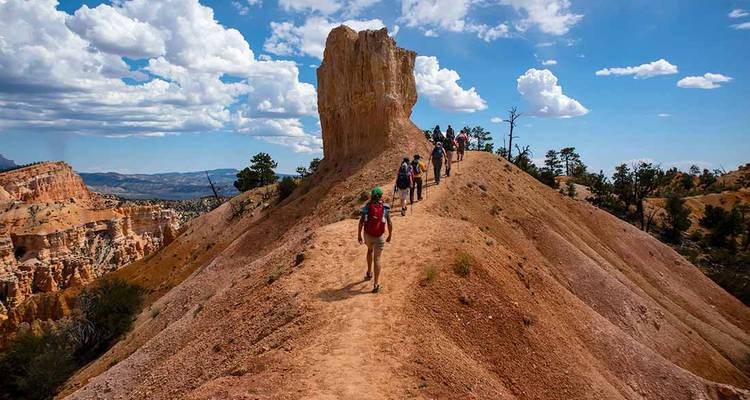Wanderer folgen einer Kammlinie an einer beeindruckenden Felssäule vorbei unter lockeren Wolken im Bryce Canyon.