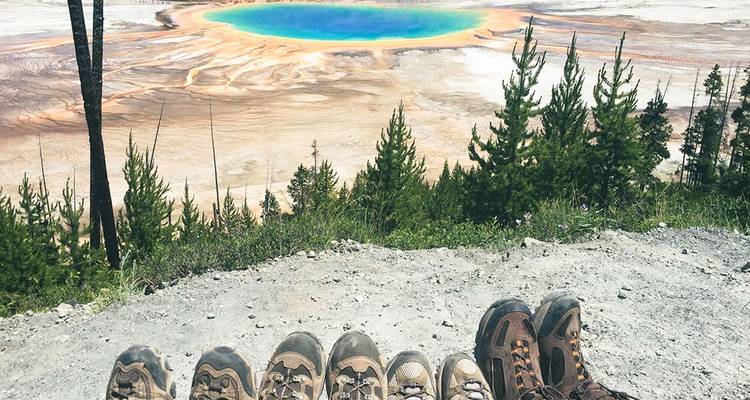 Rangée de bottes de randonneurs surplombant les couleurs arc-en-ciel du Grand Prismatic Spring aux teintes éclatantes.