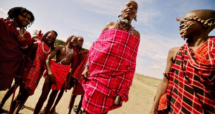 Un ancien Maasai vêtu d'un shuka aux couleurs vives se tient fièrement aux côtés des membres de sa communauté sous un ciel bleu.