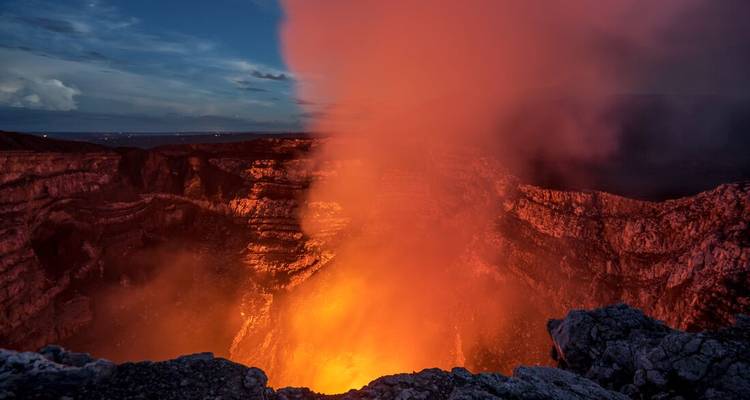 Un panache de lave brillant et dramatique s'élevant du cratère d'un volcan actif sous un ciel crépusculaire.