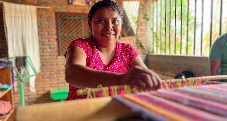 Un artisan local souriant en tissant des textiles colorés sur un métier à tisser traditionnel.