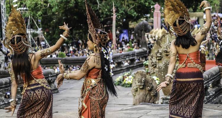 Drei traditionell gekleidete Apsara-Tänzerinnen führen einen kunstvollen Kulturtanz auf einer Freilichtbühne vor einem großen Publikum auf.
