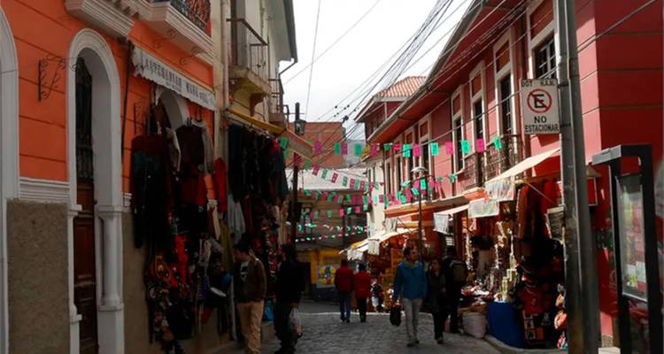 Marché de rue étroit et animé à La Paz bordé de textiles colorés, de drapeaux au-dessus, et d'acheteurs parcourant les étals.