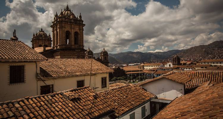 Skyline historique de Cusco avec ses toits en terre cuite et ses tours d'églises coloniales se dressant face aux montagnes des Andes.