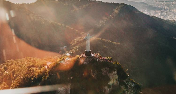 Vista aérea iluminada por el sol de la estatua del Cristo Redentor que se alza sobre la Montaña Corcovado cubierta de bosque.