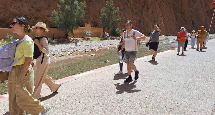 Des visiteurs se promenant le long d'un cours d'eau à la base de falaises abruptes rougeâtres sous un soleil éclatant