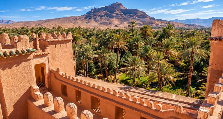 Vista desde una kasbah fortificada de adobe sobre un exuberante oasis de palmeras hacia un dramatico pico de montaña en el desierto.