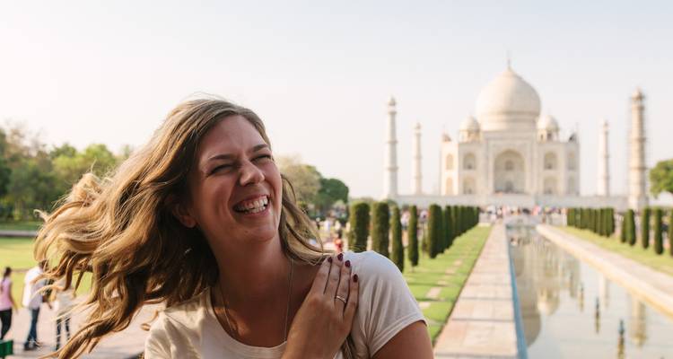 Voyageur souriant posant avec le Taj Mahal et le bassin de réflexion légèrement flou en arrière-plan.