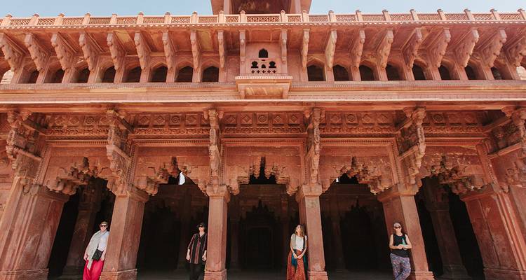 Les voyageurs explorent les colonnes de grès ornées d'une cour de palais moghol.