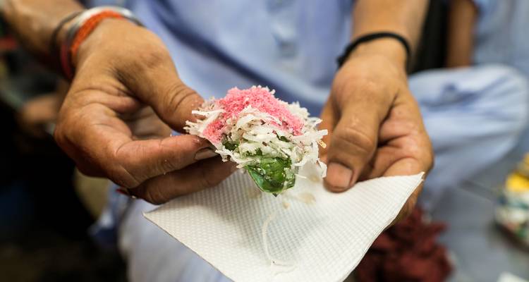 La main tient une noix de bétel colorée remplie de copeaux de noix de coco et de garniture sucrée rose vif.