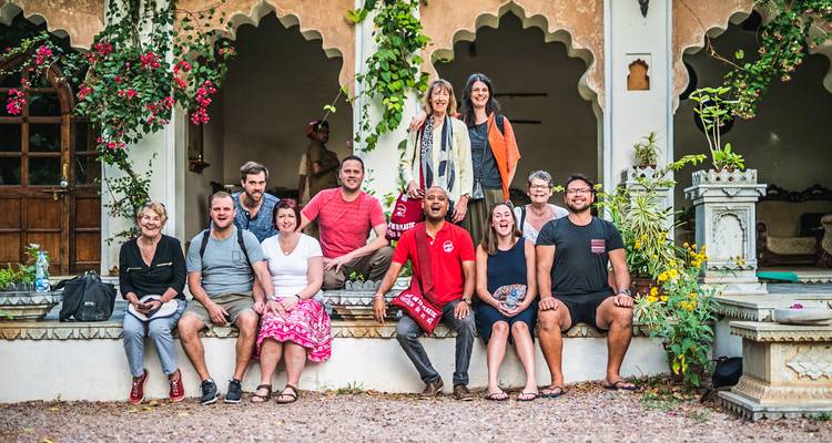 Groupe de touristes souriants posant ensemble sur un banc de cour encadré par des arches ornées et des vignes fleuries.