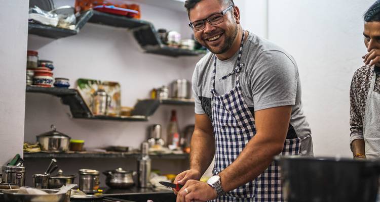 Voyageur portant un tablier sourit en hachant des ingrédients pendant un cours de cuisine.