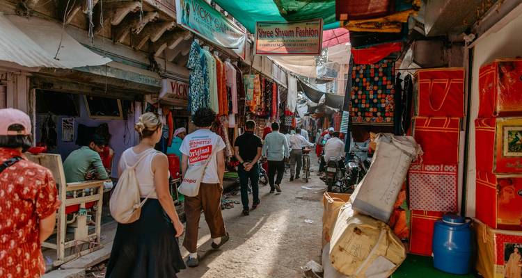 Ruelle de marché étroite et animée, bordée de boutiques de textiles colorées, avec des habitants qui se promènent et font du shopping.