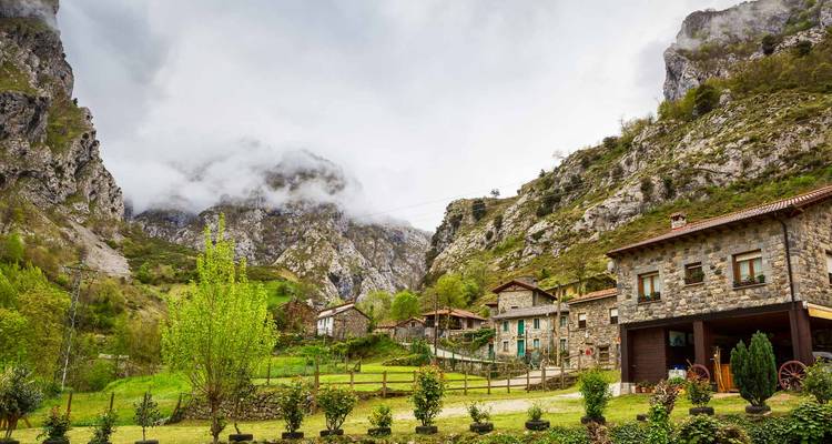 Steinerne Häuschen, die in einem üppig grünen Tal unter nebelbedeckten Klippen in den Picos de Europa eingebettet sind.