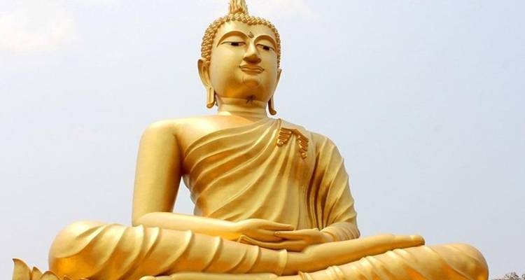 Statue de Bouddha assis dorée de grande taille sur un ciel pâle, détail de l'expression faciale sereine.