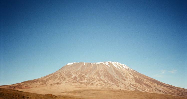 Vue panoramique du cône sommital aride du mont Kilimandjaro sous un ciel bleu dégagé.