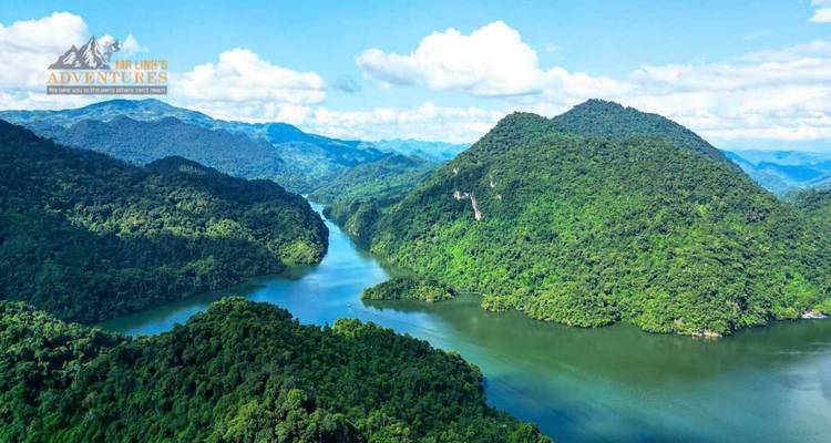 Vista aérea de un sinuoso río esmeralda atravesando densas montañas boscosas bajo cielos azules.