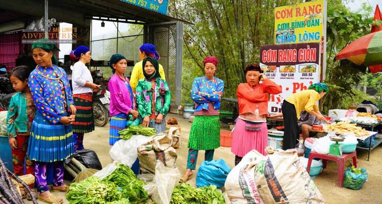 Escena vibrante del mercado de las tribus de la montaña con mujeres en faldas coloridas vendiendo verduras y productos.