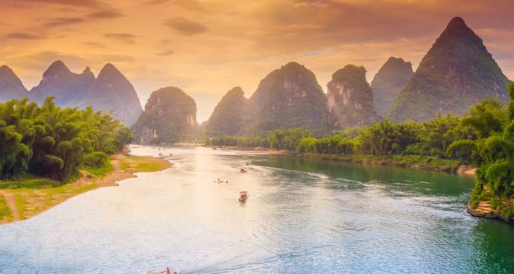 Tranquil Li River scene with karst mountains and small boats under a colorful sunset sky