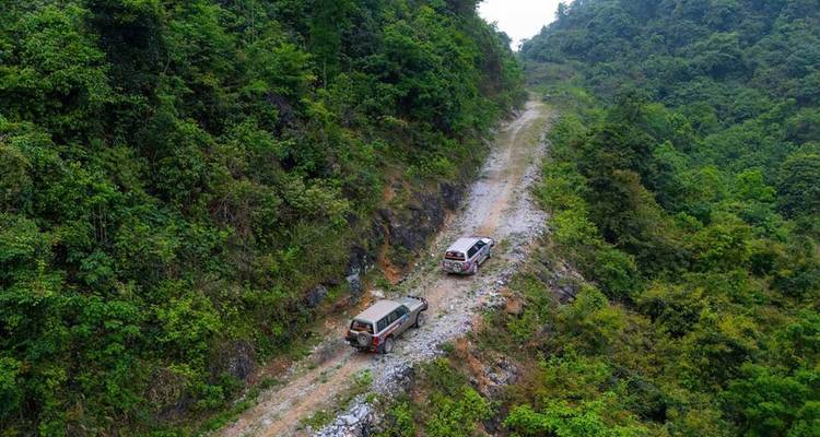 Deux véhicules 4x4 s'engagent sur un sentier de montagne rocailleux creusé dans des pentes densément boisées.