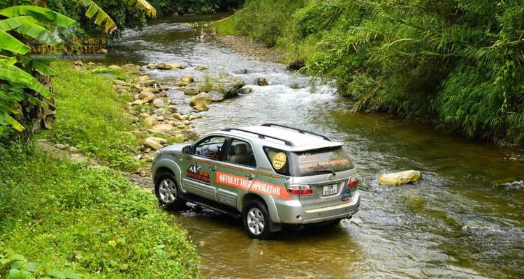 Un SUV de marque traverse en éclaboussant un cours d'eau peu profond de la jungle sur un sentier accidenté.
