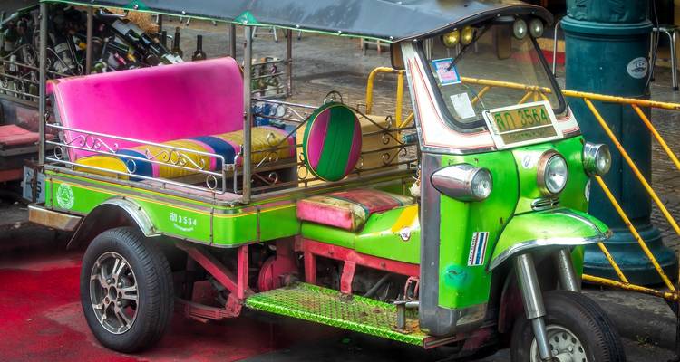 Een felgroen en roze tuk-tuk taxi wacht op een natte straat in Bangkok.