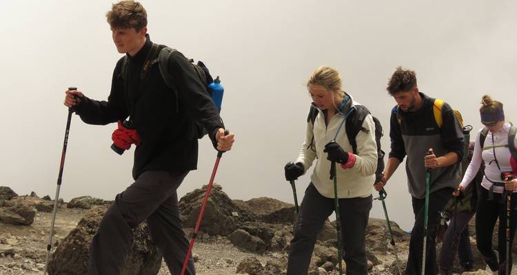 A line of hikers ascends a rocky, barren slope toward the higher reaches of Mount Kilimanjaro.