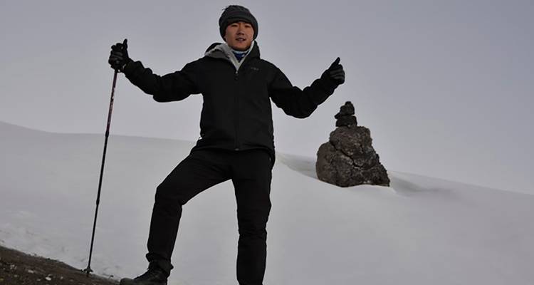 A trekker poses with poles on a snowy slope under a grey alpine sky.