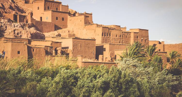 The earthen dwellings of Ait Benhaddou rise above palms and reeds in warm afternoon light.