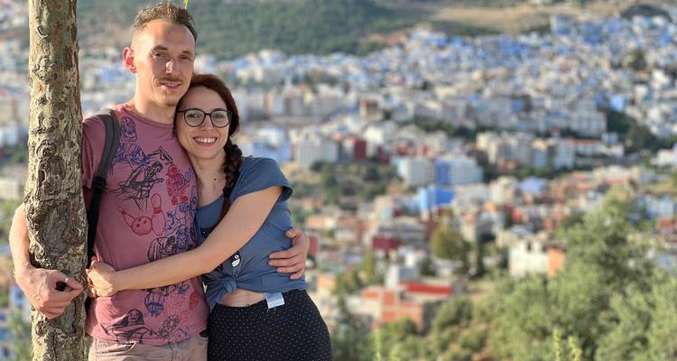 Una pareja sonriente se abraza junto a un árbol con una vista panorámica de Chefchaouen abajo.