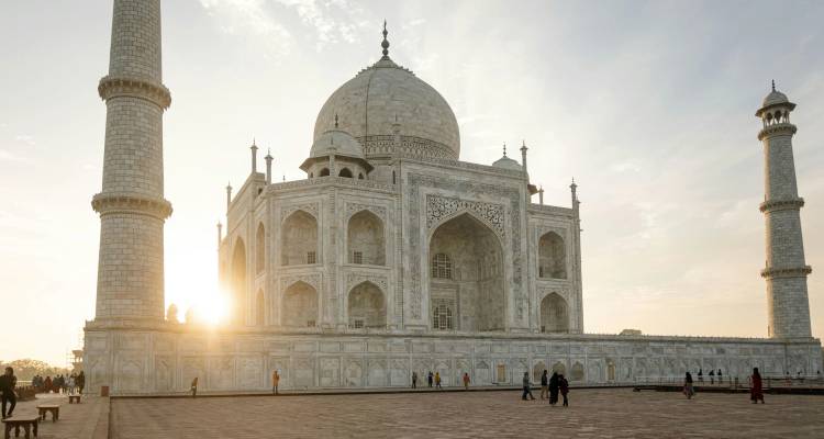 Le soleil se levant derrière le Taj Mahal en marbre blanc avec des visiteurs marchant sur la plateforme principale.