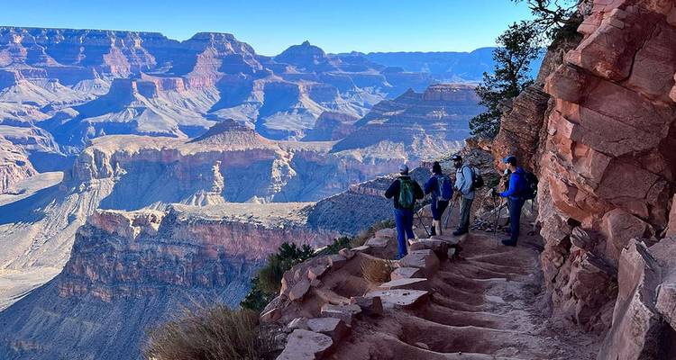 Hiking party pauses on a rugged canyon ledge to admire panoramic Grand Canyon views.