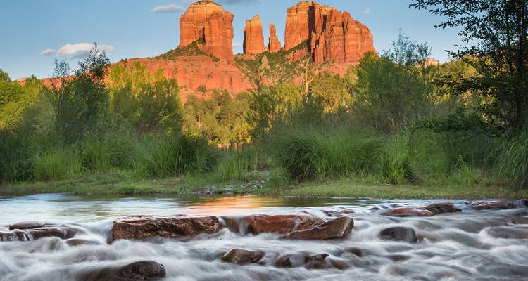 Cathedral Rock rises above a flowing creek and lush greenery in Sedona.