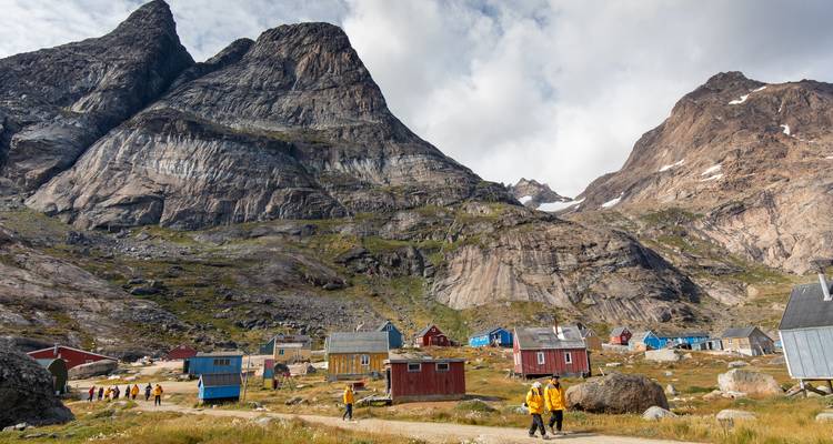 Colorful wooden cabins sit beneath towering granite peaks as yellow-jacketed travelers explore the village.