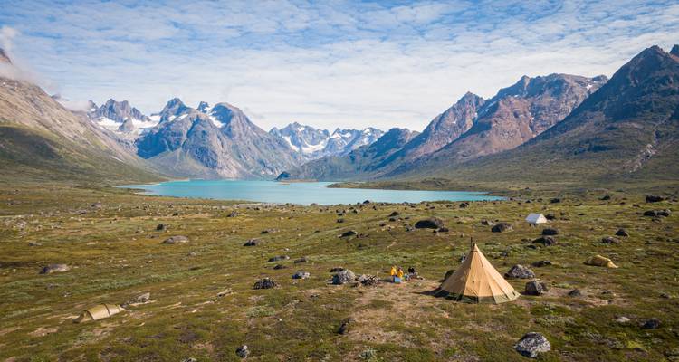 Remote tent camp overlooks a turquoise lake framed by dramatic, snow-capped peaks.