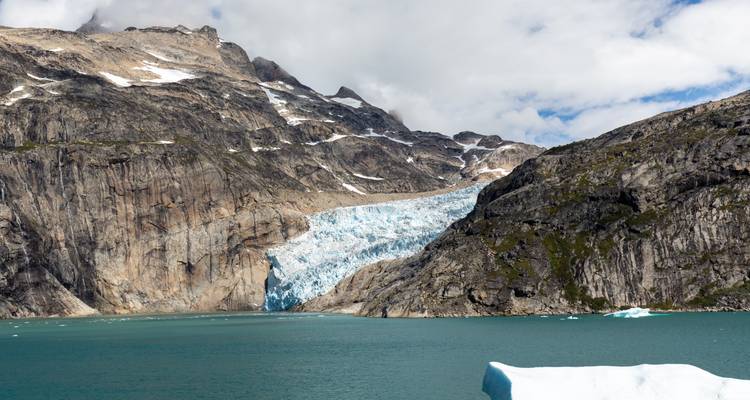 A mighty glacier spills into a teal fjord surrounded by rugged cliffs and peaks.