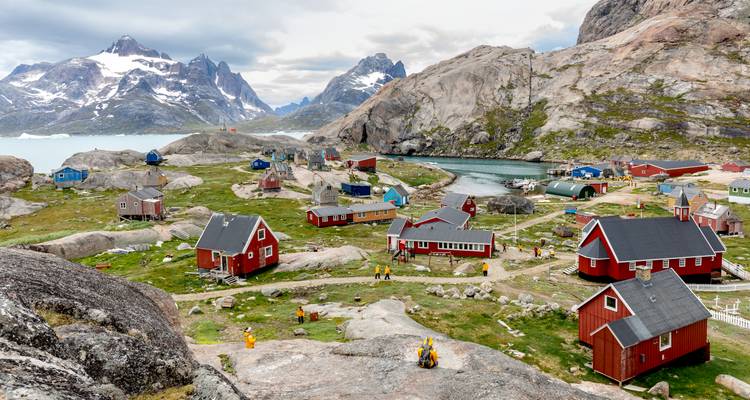 Charming red and blue houses cluster on rocky hillsides beside a fjord backed by jagged mountains.