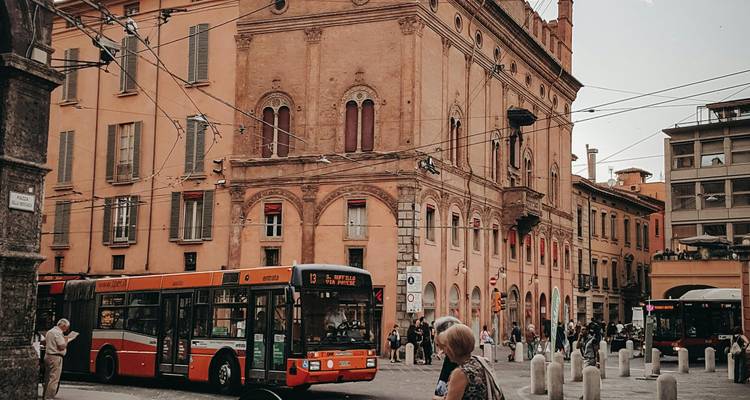 Carrefour urbain animé avec autobus municipal orange, façade de palais historique et piétons en traversée.