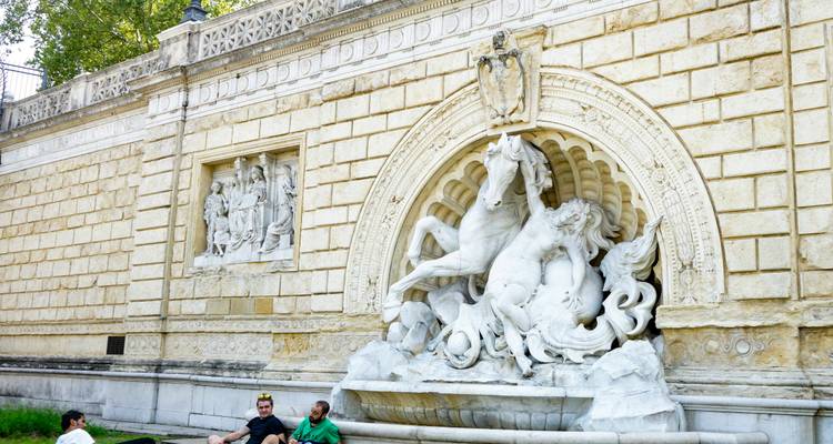 Fontaine en pierre ornée d'une sculpture de cheval cabré avec des personnes se détendant sur l'herbe à proximité.