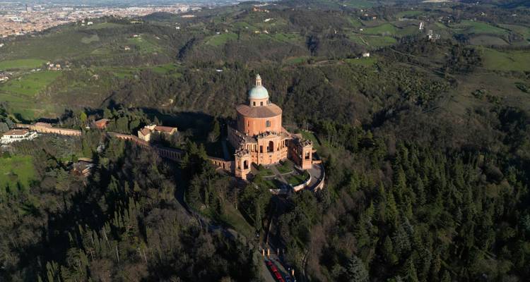 Panoramique aérien spectaculaire du Sanctuaire de la Madonna di San Luca perché sur une colline boisée avec la campagne vallonnée s'étendant au-delà.