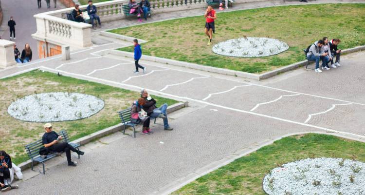 Vue aérienne d'un jardin de place avec des bancs et de petits groupes de personnes assises sur l'herbe.