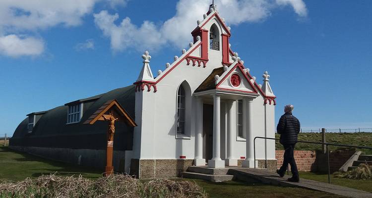 La chapelle italienne ornée se dresse sur un ciel bleu éclatant tandis qu'un visiteur l'observe.