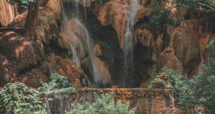 Close-up of moss-covered limestone where slender waterfalls trickle down orange rock walls.
